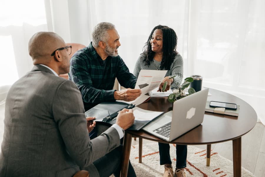 Financial planning with couple and professional in office over paperwork and laptop