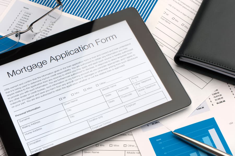 Online mortgage application on digital tablet with papers in background